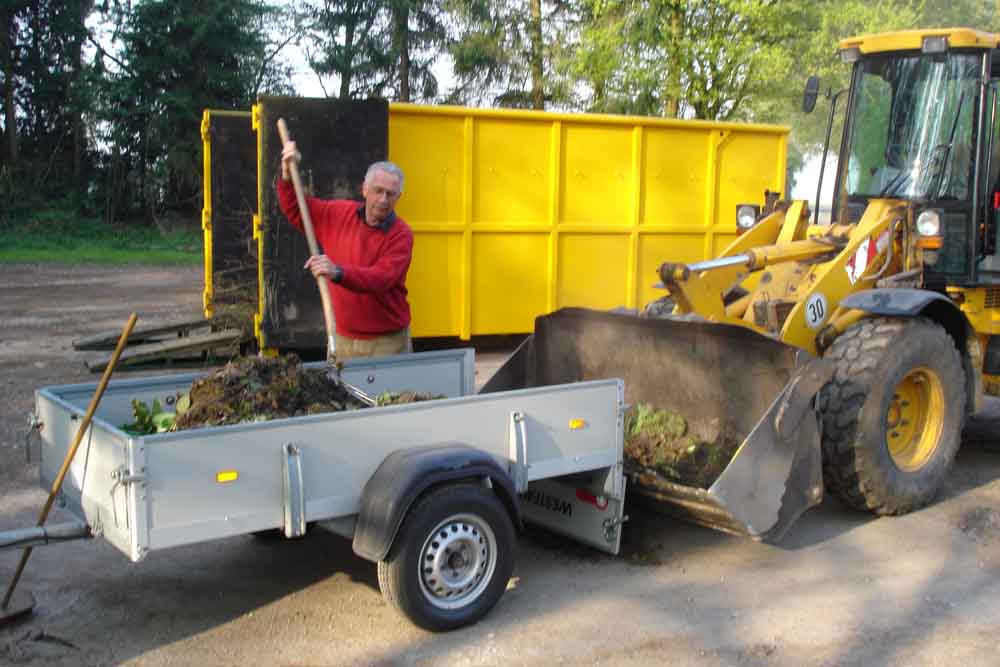 Mann lädt Grünabfälle auf Anhänger
