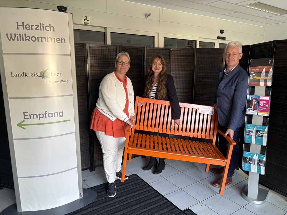 Landrat Matthias Groote, Elke Engels (Gleichstellungsbeauftragte des Landkreises Leer) und Tomke Hamer (Gleichstellungsbeauftragte der Stadt Leer) tragen die Orangene Bank in den Vorraum des Kreisgebäudes in der Bavinkstraße