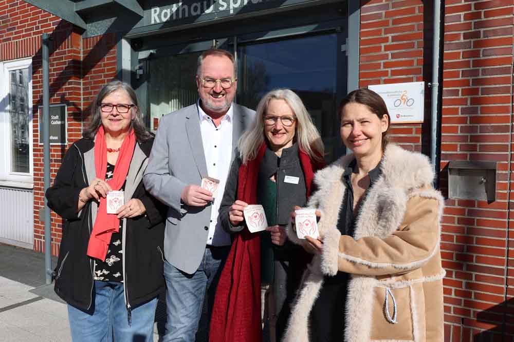Heike Bach (Stadt Cuxhaven) und Oberbürgermeister Uwe Santjer brachten gemeinsam mit Marian Breuer und Mariana Härtel (Der Paritätische Cuxhaven) die Aufkleber am Rathaus an