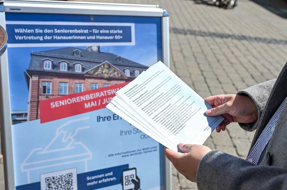 Person mit Infomaterial vor Infoplakat