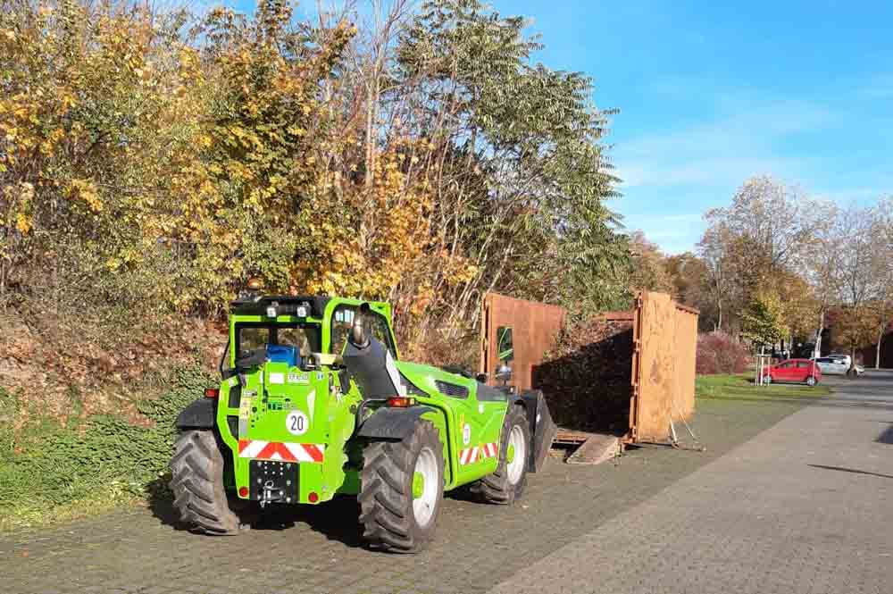 Bagger vor einem Container mit Grünabfällen