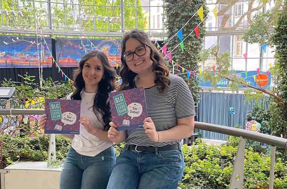 Hannah Kiel (l.) und Katharina Kirschner von der Stadtbibliothek Herten präsentieren den diesjährigen Flyer des Sommerleseclubs