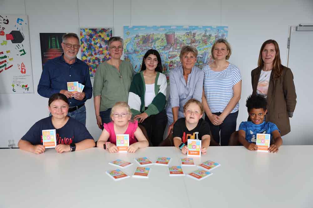 Maria (9), Emily (7), Lorenz (8) und Djibril (9) präsentieren gemeinsam mit (von hinten links) dem Vorsitzenden des Jugendhilfeausschusses Norbert Enters, der stellvertretenden Landrätin Heike Bartmann-Scherding, Nurten Özkaya vom Treffpunkt Villa, Sachgebietsleiterin Kinder- und Jugendförderung Ilka Essers, Yvonne Rome vom Treffpunkt Windmühle und Angela Troeßer vom Go In den Ferienspaß 2026