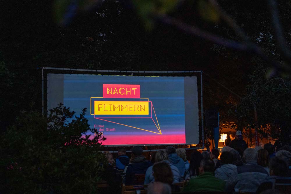 Menschen sitzen abends vor einer großen Leinwand