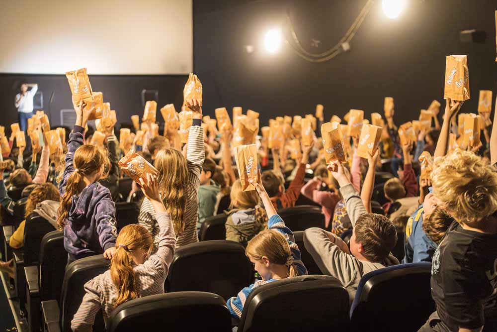 Kinder sitzen im Kino und halten Popcorn hoch