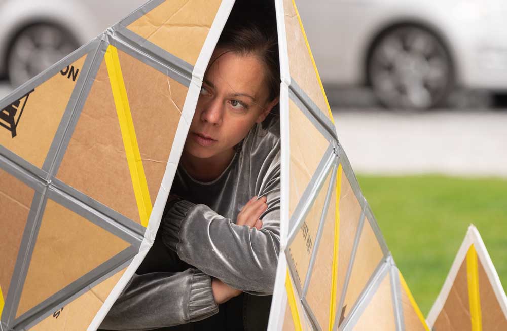 Frau sitzt in einem Zelt aus Pappe