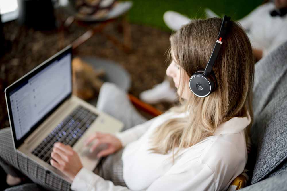Frau mit Kopfhörern sitzt vor einem Laptop