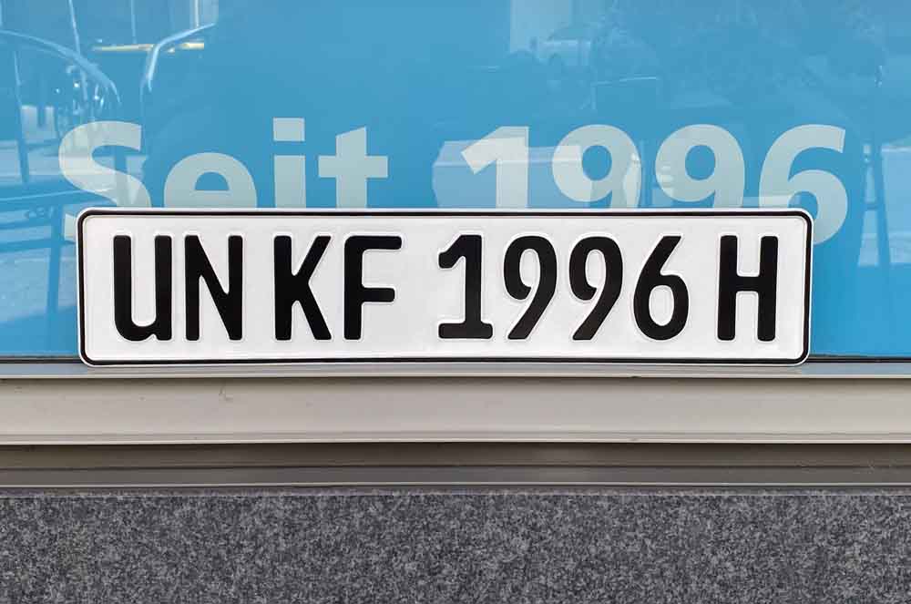 Autokennzeichen mit dem Aufdruck "UN KF 1996 H" lehnt an einem Fenster
