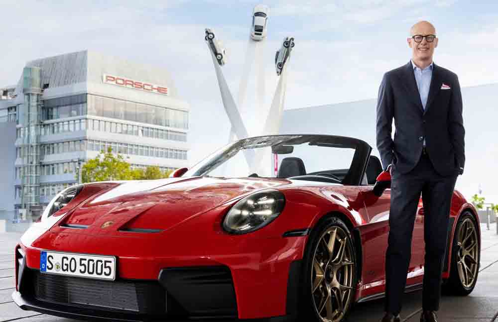 Dr. Michael Leiters steht neben einem Porsche, vor der Zentrale von Porsche